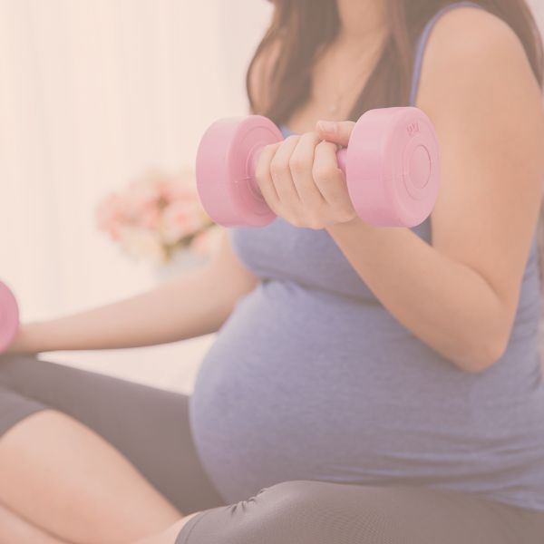 Close-up of a pregnant woman in workout clothes holding pink dumbbells during a prenatal strength exercise.